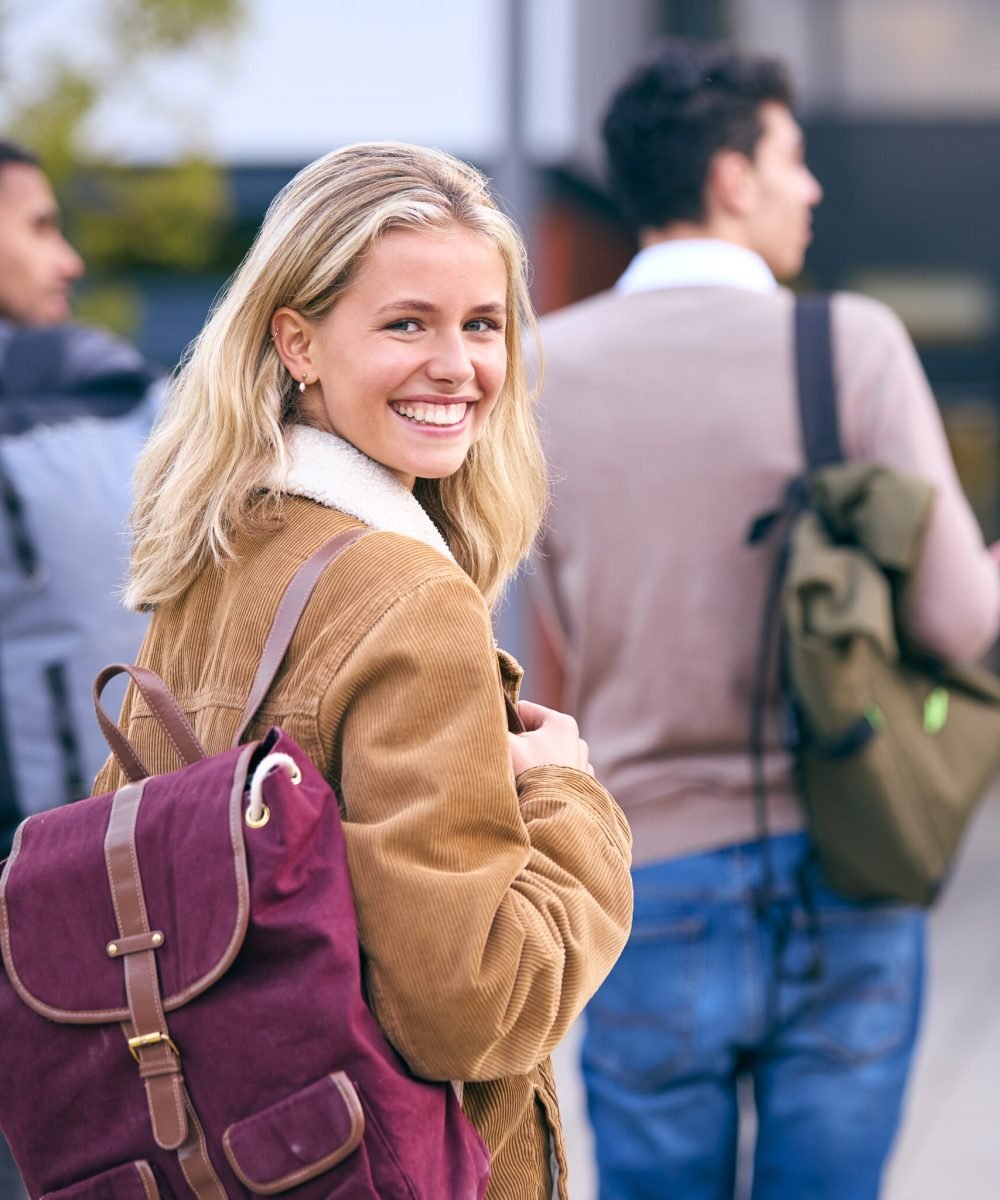 Portrait Of Female University Student Looking Over Shoulder With Friends Outside College Buildings